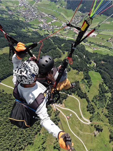 A tandem paragliding flight over green hills and valleys. In the background, small villages and a vast landscape can be seen.