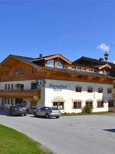 A rustic building in alpine style with several floors and a beautiful outdoor area. The hotel is situated in a picturesque setting with a clear blue sky.