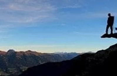 A person stands with a dog on a rock, gazing at the vast landscape. The sky is clear and the mountains are visible in the background.