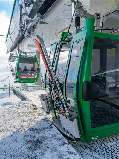 Eine modernisierte Gondelbahn in einer schneebedeckten Berglandschaft. Im Hintergrund sind weitere Gondeln zu sehen, die in die Höhe fahren.