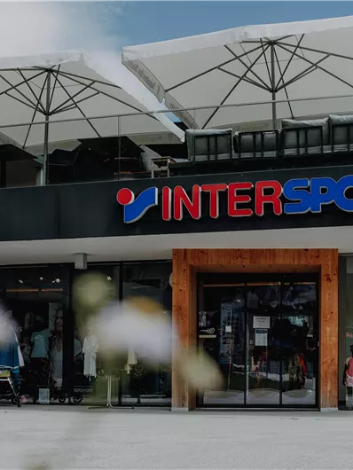 Ein modernes Geschäft von INTERSPORT mit einer großen Glasfront. Über dem Eingang sind Sonnenschirme aufgestellt.