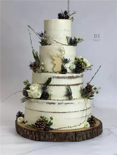 Een elegante taart met meerdere lagen, versierd met bloemen en dennenappels. Bovenop bevindt zich een hert-ontwerp van hout.