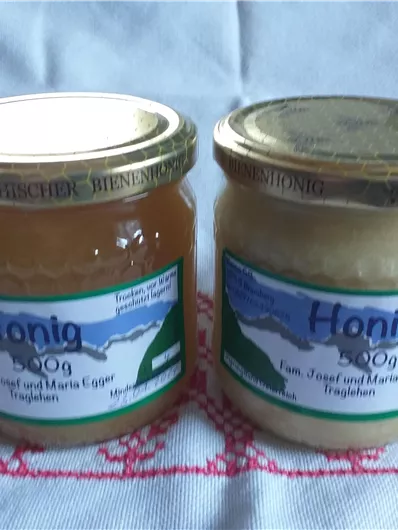 Zwei Gläser Honig stehen auf einem Tisch. Eines ist hell und das andere dunkel, beide mit Etiketten versehen.