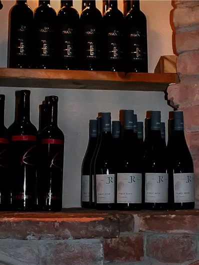 A wine collection on a rustic shelf. The bottles are arranged in various positions and display different labels.