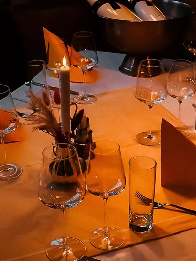 An elegantly set table with orange napkins and candlelight. The glasses and cutlery are thoughtfully arranged.