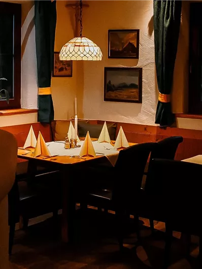 A cozy restaurant with a set table. The light is warm and inviting, while the windows offer a view outside.