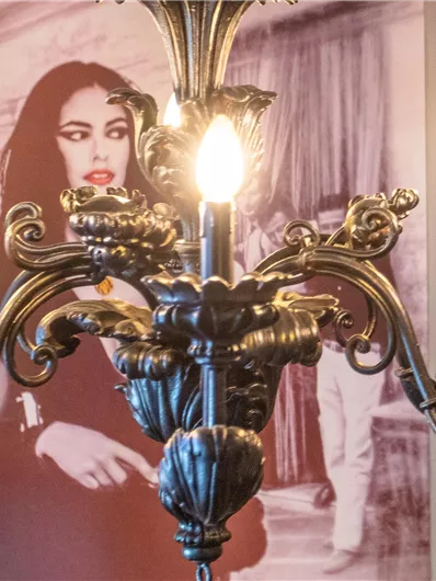 An elegant chandelier with glowing candles. In the background, there is a picture of a woman.