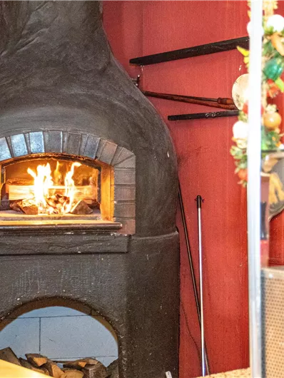 A traditional wood oven in a restaurant, filled with flames. The surroundings are designed in warm shades of red.