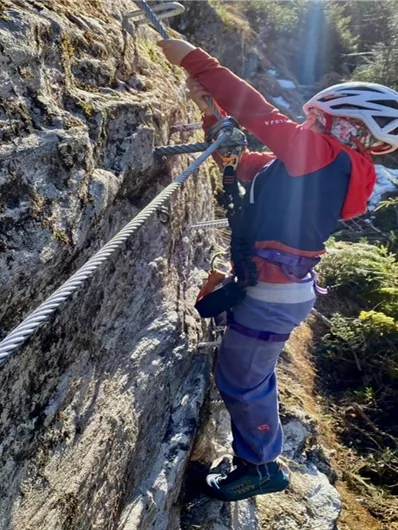 Ein Kind klettert an einer Felswand in der Natur. Die Umgebung ist grün und sonnig.