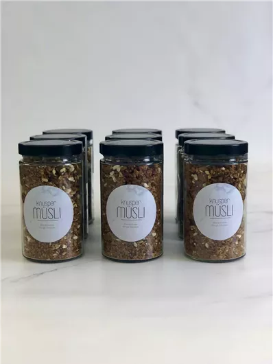 Meerdere glazen met muesli zijn op een tafel geplaatst. Elk glas is helder en heeft een eenvoudig etiket met de tekst "Krüger Muesli".
