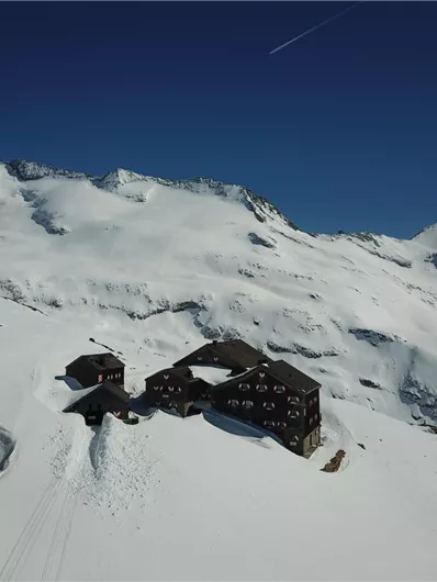 Een schilderachtige berghut omringd door besneeuwde bergen. De heldere blauwe lucht zorgt voor een rustige winterse sfeer.