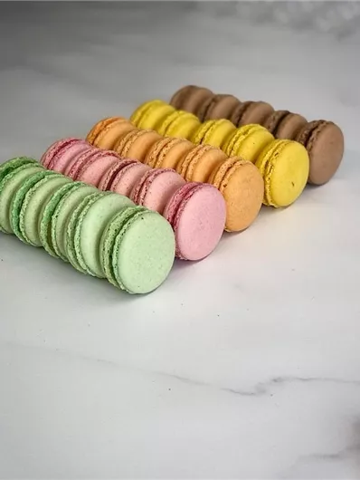 Kleurige macarons in verschillende kleuren liggen in een rij op een witte oppervlakte. De zoetigheden zijn in harmonieuze kleurtinten gerangschikt en zien er smakelijk uit.
