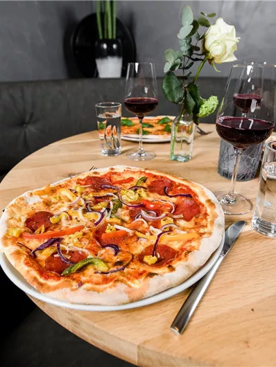 Een heerlijke pizza met verschillende toppings op een ronde tafel. Op de achtergrond zijn glazen en een bloeiende plant te zien.