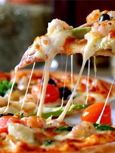 A delicious pizza with melting cheese, tomatoes, seafood, and vegetables. The cheese stretches and is tasty when pulling out the slices.