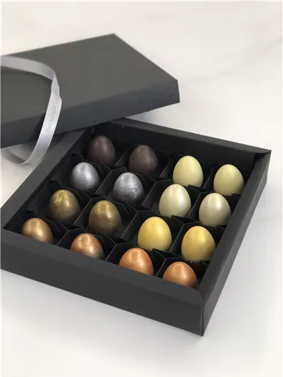 Een elegante doos met 16 chocolade-eieren in verschillende kleuren. De eieren zijn kunstvol gerangschikt en hebben een feestelijke uitstraling.