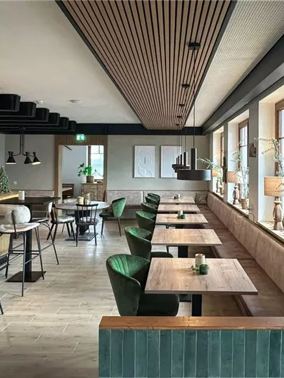 Een modern restaurant met een gezellige sfeer. Er zijn houten panelen, groene stoelen en decoratieve elementen aan de muur.