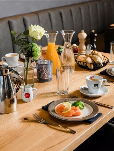 Een mooi gedekte tafel met ontbijtaanbiedingen zoals zalm, broodjes en vers fruit. Veel drankjes en decoraties maken het beeld compleet.