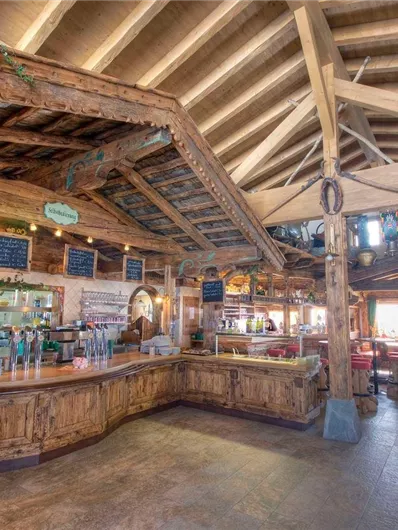 Een rustiek restaurant met houten meubels en een uitnodigende bar. Grote ramen laten veel licht binnen en creëren een gezellige sfeer.
