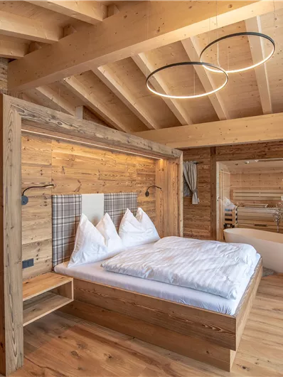 Een moderne slaapkamer met een houten bed en witte beddengoed. De ruimte heeft een heldere sfeer met houten plafonds en een mooi uitzicht op de natuur.