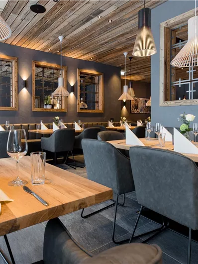 Een elegant restaurant met moderne meubels en warme verlichting. De tafels zijn mooi gedekt en bloemen sieren de ruimte.