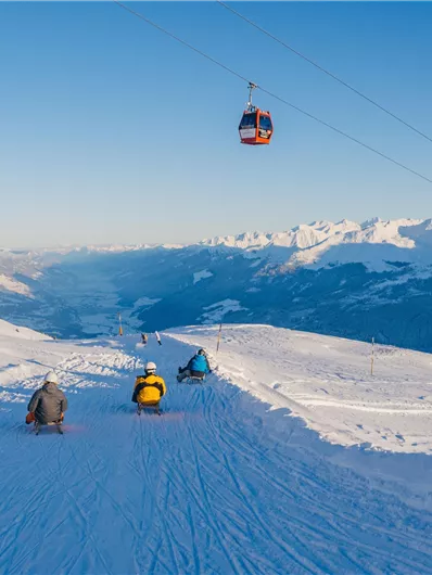 Eine winterliche Berglandschaft mit schneebedeckten Hängen. Im Hintergrund schwebt eine Gondel über die Berge.