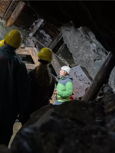A group of people wearing hard hats stands in a cave. In the foreground, someone is explaining something to the others.