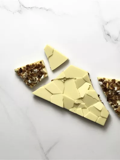 Een stuk witte chocolade dat in onregelmatige stukken is gebroken. Sommige stukken zijn versierd met noten en andere ingrediënten.