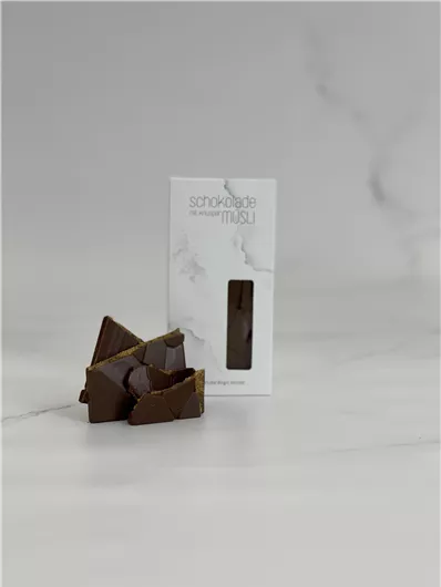 Een pakket met chocoladeg sweets en enkele stukken chocolade liggen ernaast. De achtergrond is helder en neutraal.