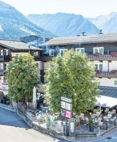 A charming hotel with several floors, surrounded by trees and mountains. The facade is tastefully decorated and offers an inviting outdoor area.