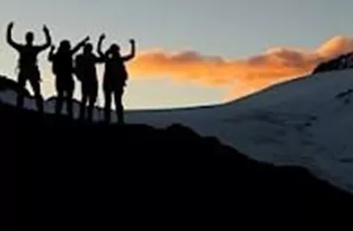 Eine Gruppe von Wanderern steht silhouettiert gegen den Sonnenuntergang. Hinter ihnen sind Berge und Schnee zu sehen.