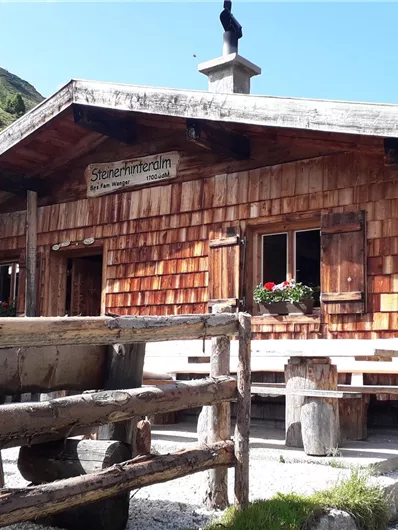 Eine schöne Almhütte aus Holz mit einem traditionellen Dach. Im Hintergrund sind sanfte, grüne Hügel zu sehen.