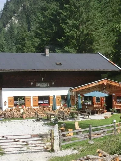 Een gezellige berghut omringd door mooie bomen. Het buitengedeelte heeft tafels en stoelen met parasols.