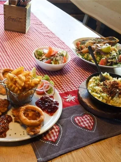 A feast with various dishes on a table. There are fries, salad, a main dish with meat and sauce, and a small pan with a side dish visible.