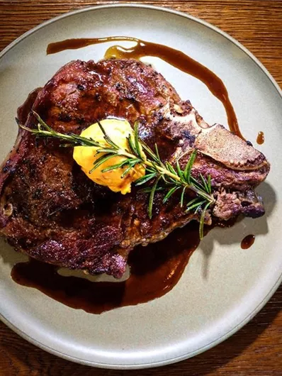 A juicy piece of meat on a plate, garnished with fresh rosemary and a piece of butter. Additionally, some sauce on the plate.