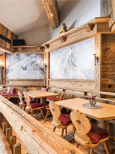 Ein gemütliches Restaurant im rustikalen Stil mit Holzmöbeln und großen Fenstern. Die Wände sind mit ansprechenden Bildern von Berglandschaften dekoriert.