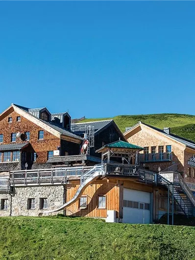 Ein gemütliches Berghaus auf einer grünen Wiese. Im Hintergrund ist ein klarer blauer Himmel zu sehen.