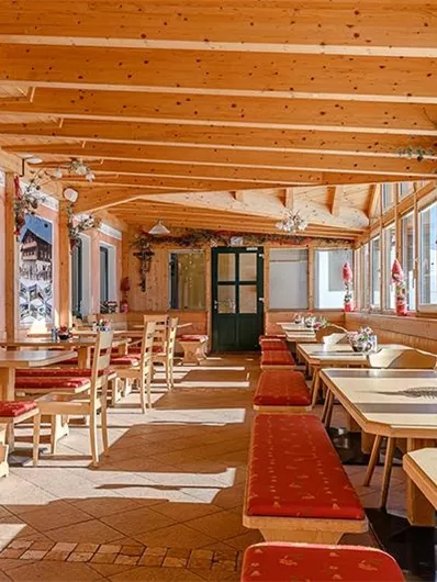 A cozy interior with a wooden beam ceiling and large windows. The tables and benches are rustic and create an inviting atmosphere.