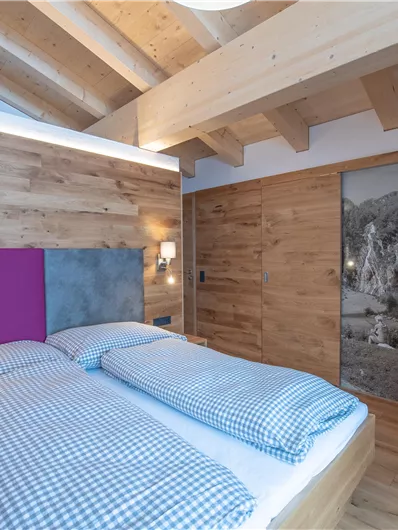 Een moderne slaapkamer met houten muren en een gezellig tweepersoonsbed. Het plafond is open en er is een kleine werkplek met een stoel.