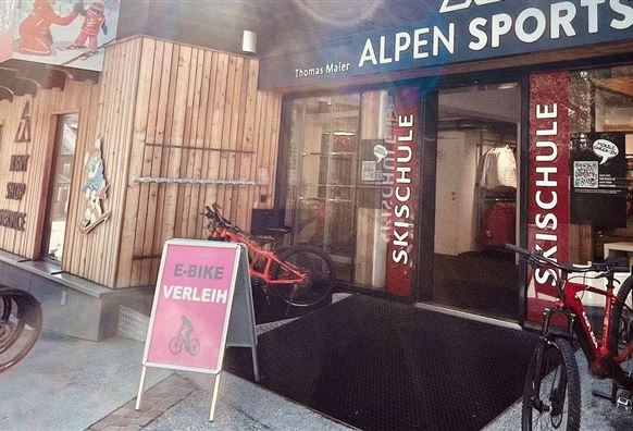 A store called "Alpen Sports" with offers for ski school and bicycles. Several bicycles and a sign are in front of the store.