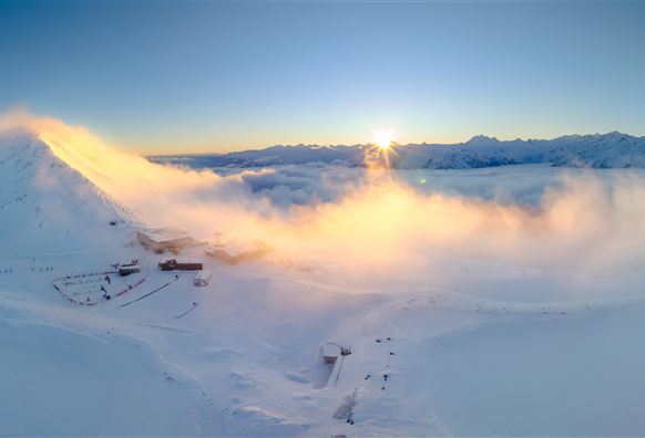 Eine beeindruckende Winterlandschaft mit schneebedeckten Bergen und einem wunderschönen Sonnenaufgang. Sanfte Wolken schweben über der verschneiten Landschaft.