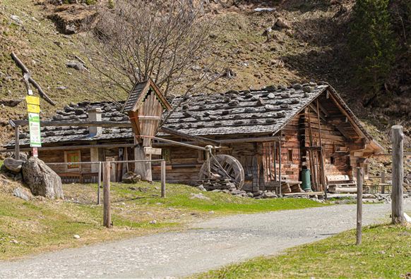 Ein rustikales Holzhaus mit einem Wasserfall-Mühle und einem grünen Garten. Die Landschaft ist von sanften Hügeln geprägt.