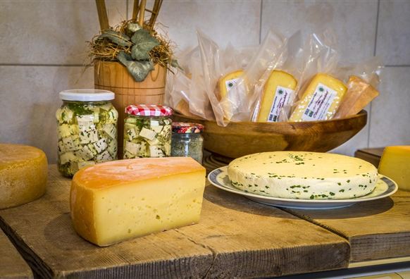 Eine Auswahl an verschiedenen Käsesorten auf einem Holztisch. Im Hintergrund sind eingelegte Käse und Verpackungen sichtbar.