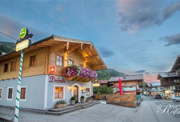 Ein traditionelles alpenländisches Gasthaus mit blühenden Balkonblumen. Der Abendhimmel zeigt sanfte Farben über der ruhigen Straße.
