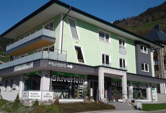 Ein modernes Gebäude mit einer grünen Fassade und großen Fenstern. Im Erdgeschoss befindet sich ein Skiverleih.