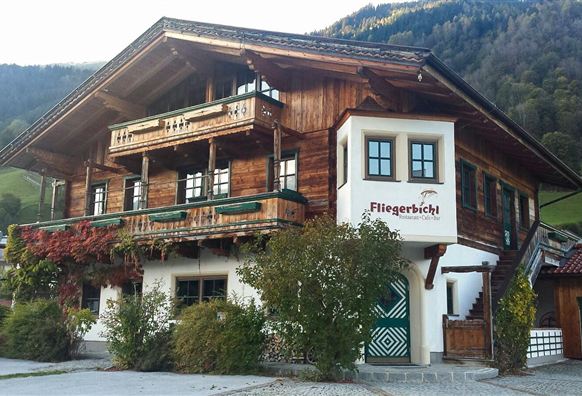 Eine traditionelle Almhütte mit Holzfassade und mehreren Balkonen. Umgeben von Bäumen und Bergen, strahlt sie ländlichen Charme aus.