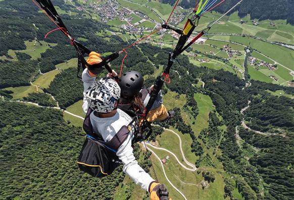 A tandem paragliding flight over green hills and valleys. In the background, small villages and a vast landscape can be seen.