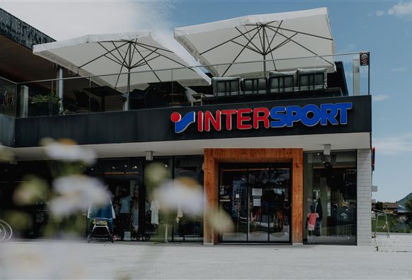 A modern store by INTERSPORT with a large glass front. Above the entrance, umbrellas are set up.