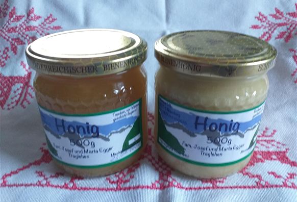 Zwei Gläser Honig stehen auf einem Tisch. Eines ist hell und das andere dunkel, beide mit Etiketten versehen.