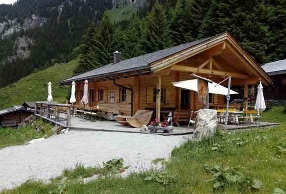 A cozy wooden mountain hut with a terrace and sun umbrellas. Surrounded by green meadows and mountains, it is an ideal place to relax.