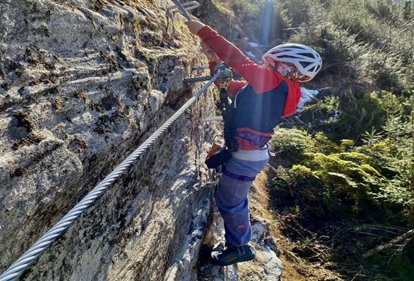 A child is climbing on a rocky wall in nature. The surroundings are green and sunny.